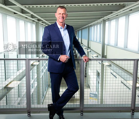 Professional Photographer Houston Business executive standing on a modern office hallway during a personal branding photography session by Houston Personal Branding Photographer Michael Carr Photography.